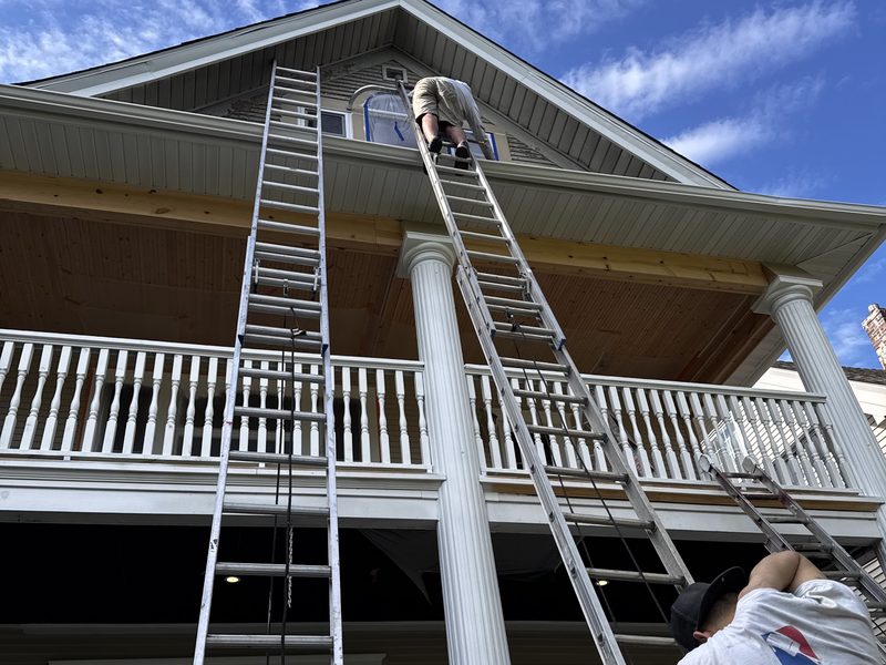 Painters coating the upper exterior of a two-story home