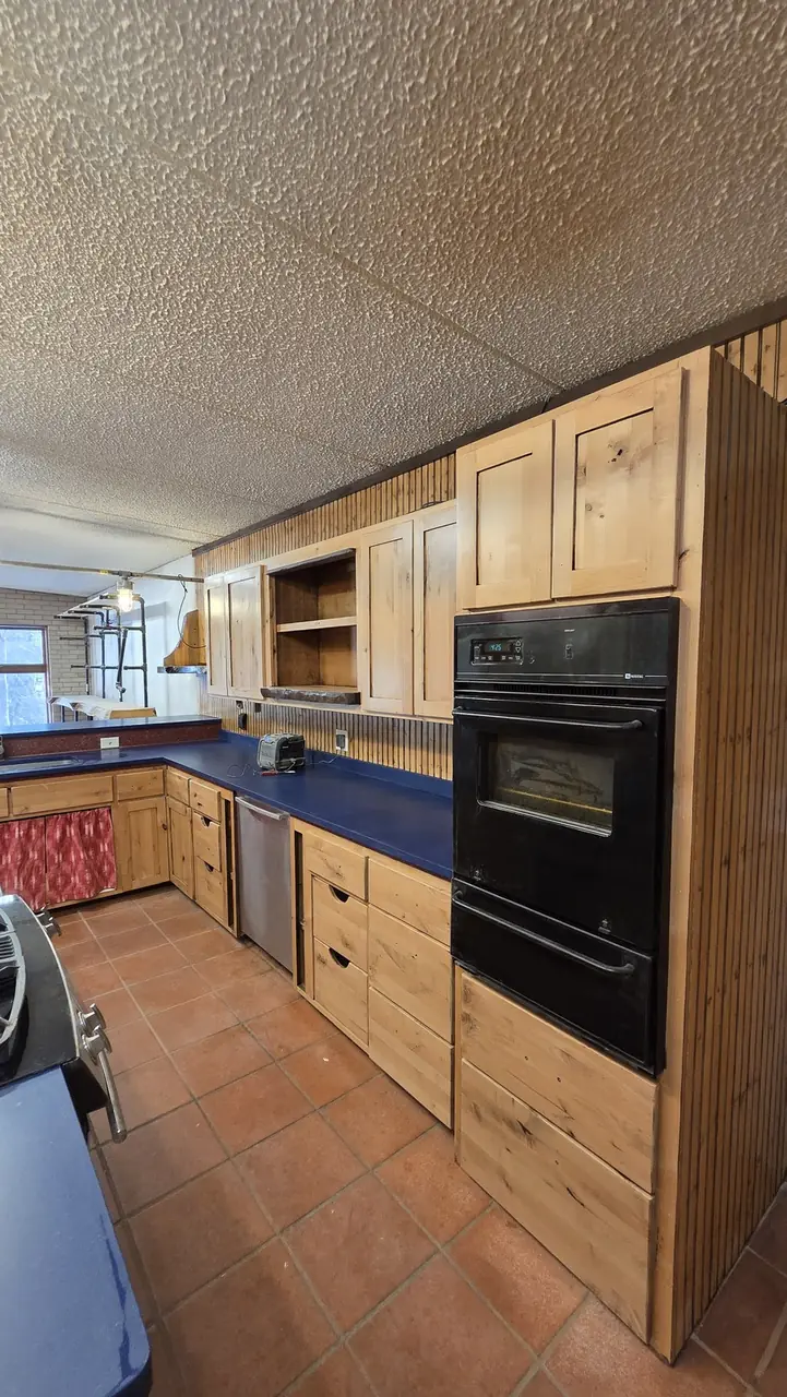 Wall of knotty pine kitchen cabinets with a built-in oven and blue countertops