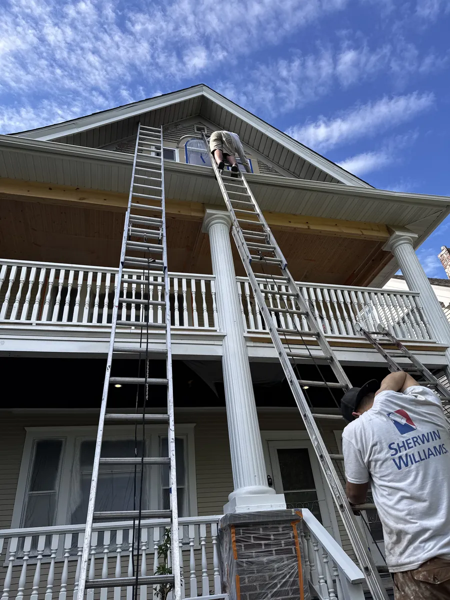 Two painters on extension ladders finishing porch columns and dormer trim on a large two-story home