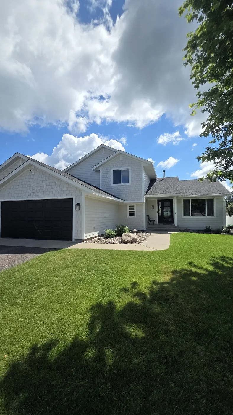Two-story home with freshly painted cream shake siding and a black front door and garage door