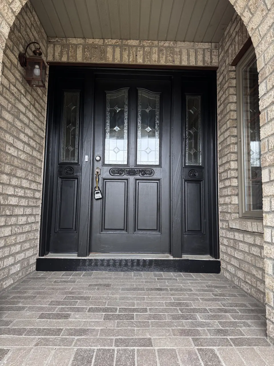 Freshly painted black front door with glass panels and brick surround