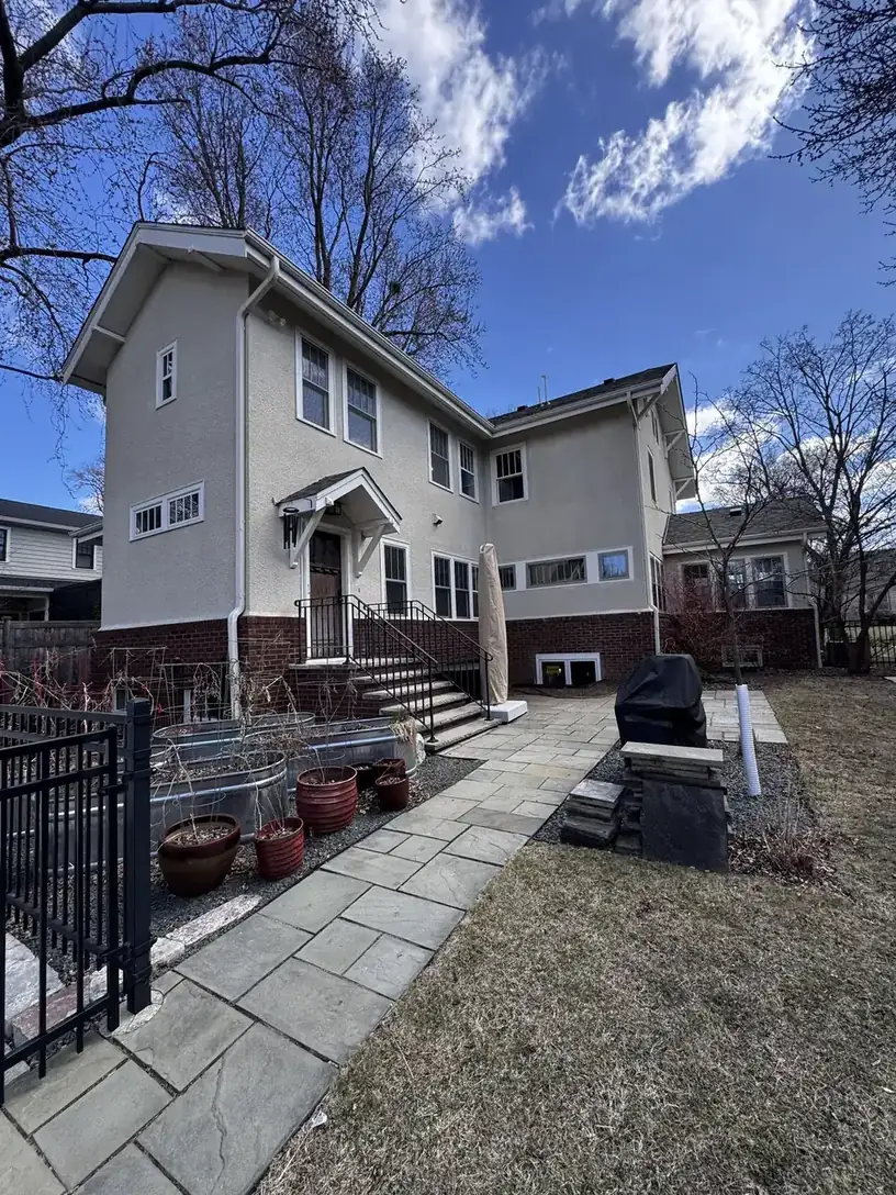 Two-story stucco and brick home exterior with a paver walkway and patio