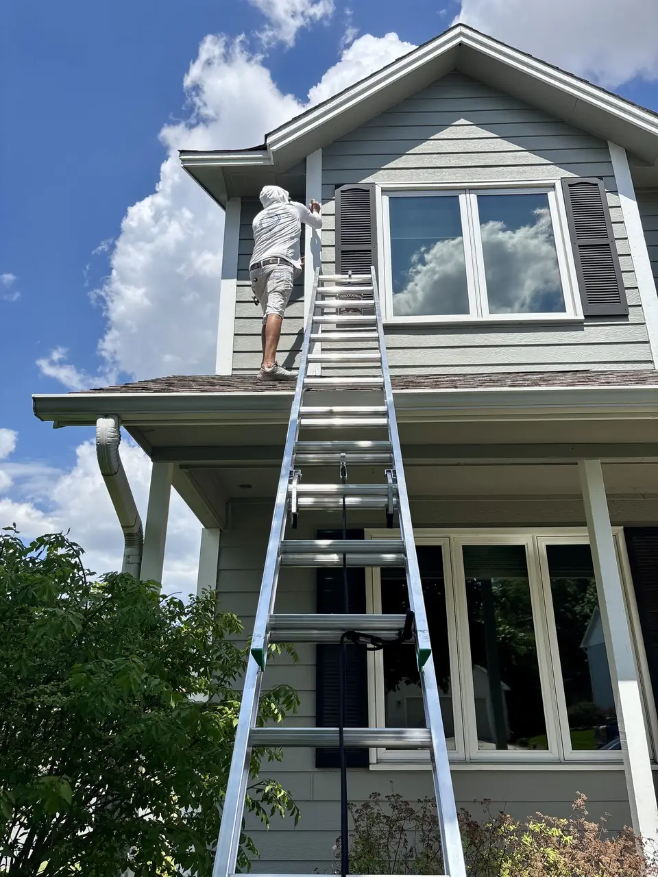 Painter on an extension ladder finishing the upper gable of a two-story home