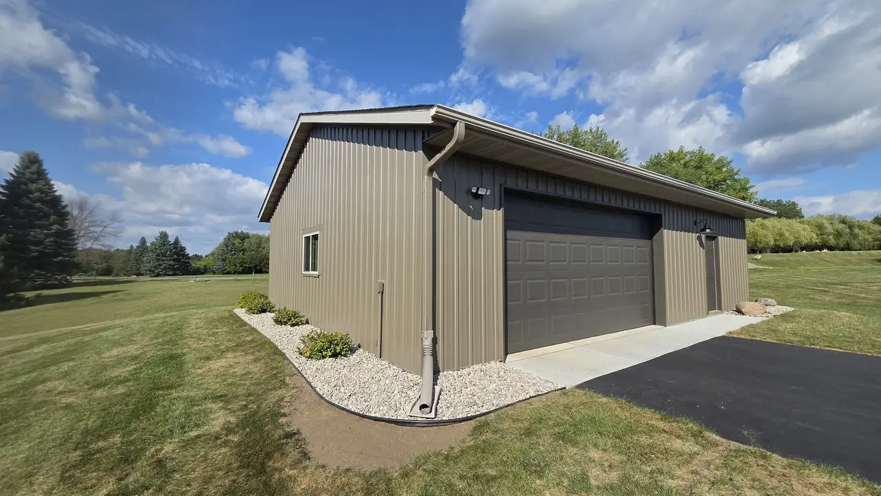 Detached garage building with tan metal siding and a dark garage door