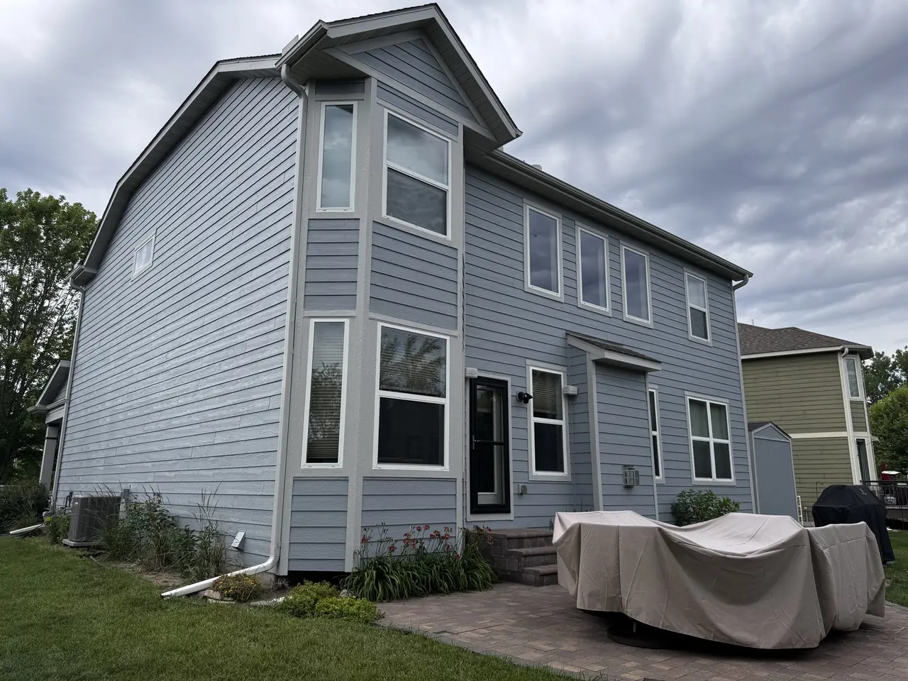 Rear exterior of a two-story home with freshly painted blue-gray siding and a covered patio