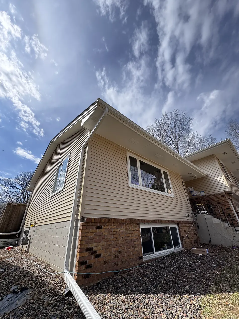 Close-up of freshly painted tan vinyl siding and brick foundation