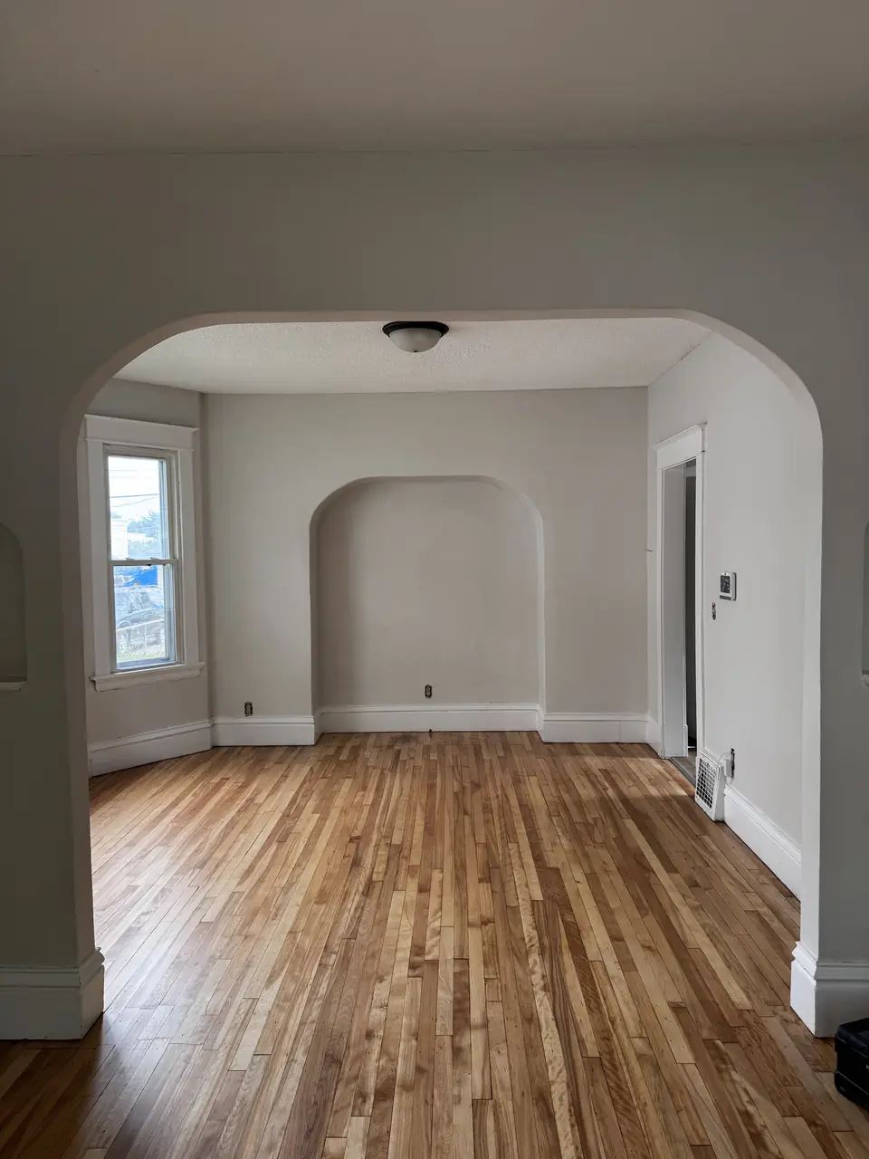 Empty room with fresh white walls, an arched doorway and refinished hardwood floors