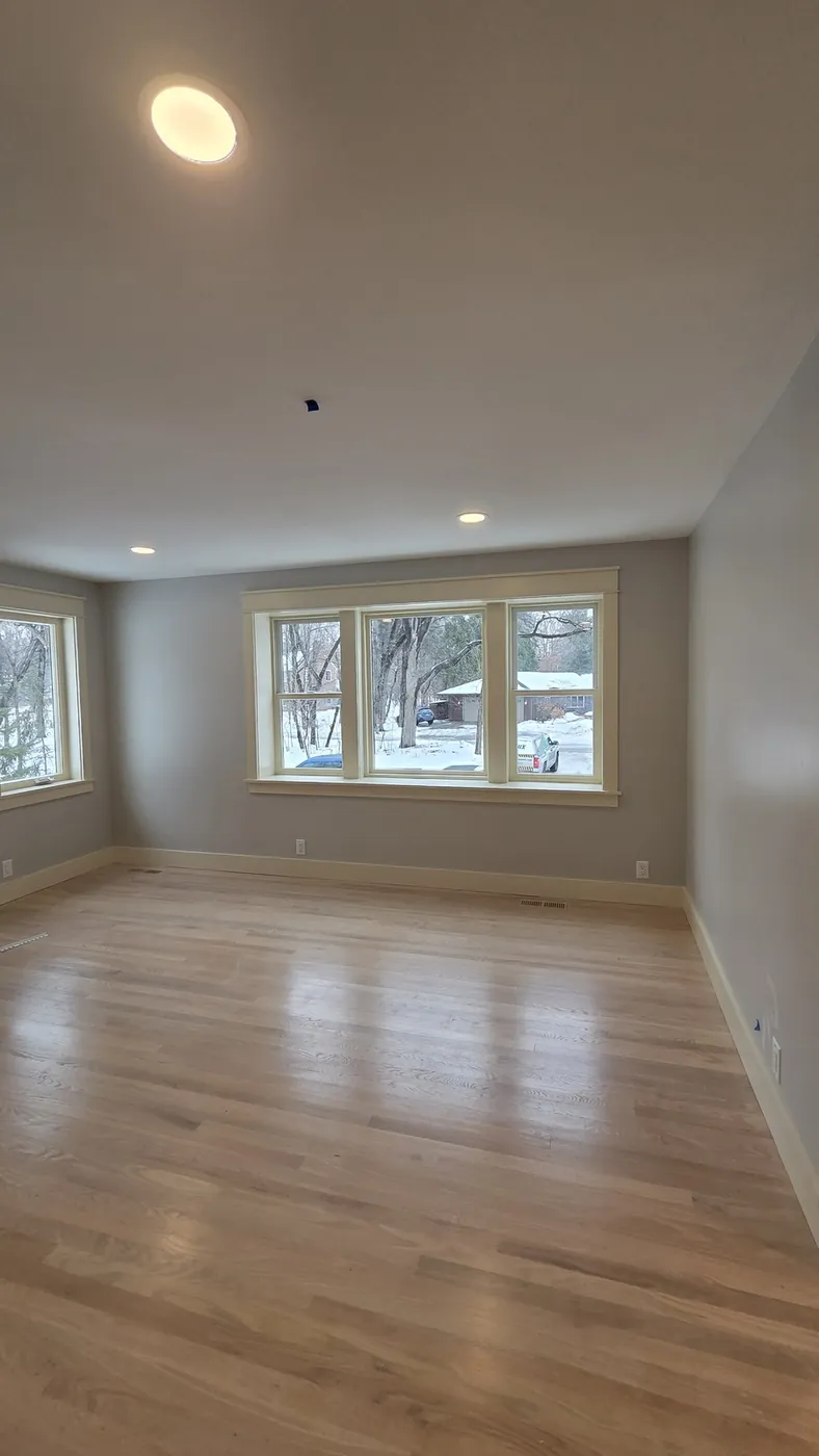 Empty living room after painting, with fresh gray-taupe walls, white trim, and refinished hardwood floors