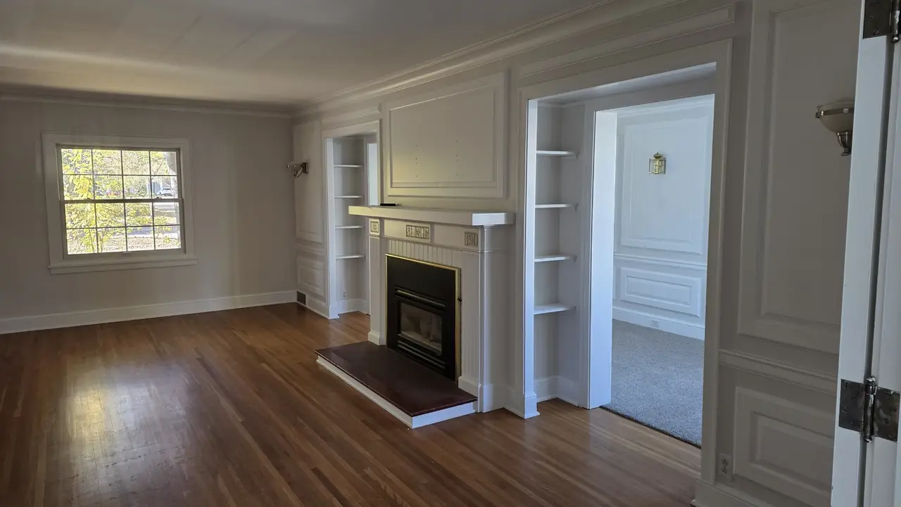 Freshly painted living room with white built-in shelving, a tiled fireplace surround and refinished hardwood floors