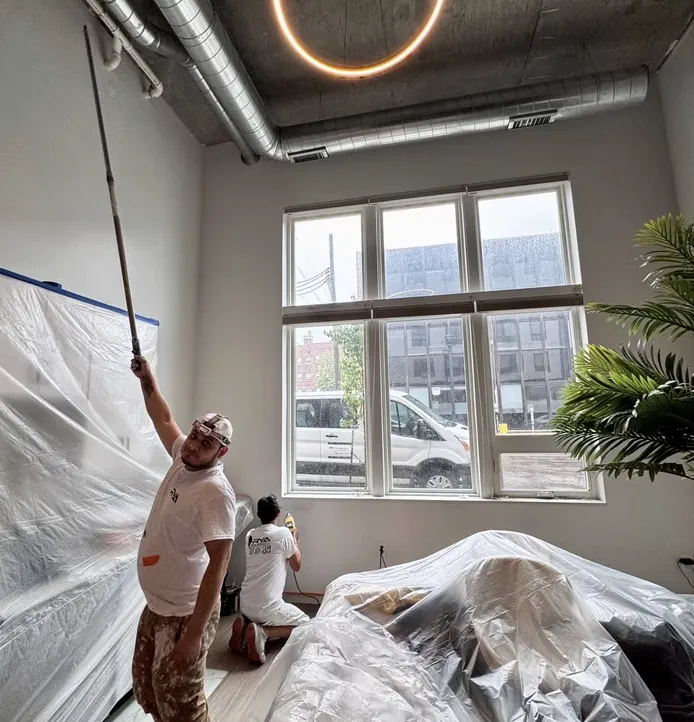 Painter on a ladder prepping a commercial interior ceiling with plastic sheeting