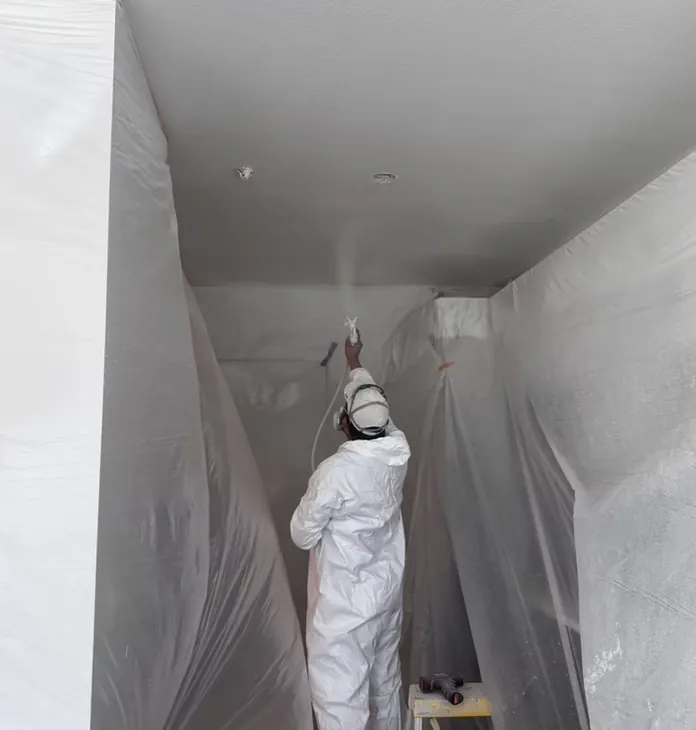 Painter in full protective gear spray finishing a ceiling and stairwell