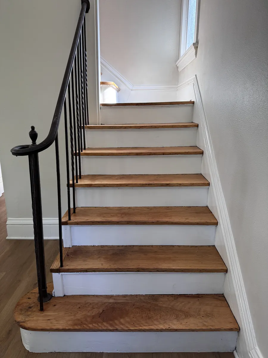 Staircase with newly refinished wood treads and freshly painted white risers and railing trim