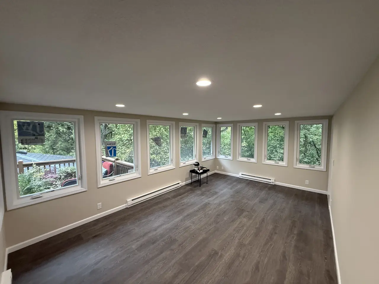 Corner view of a freshly painted sunroom with multiple windows and recessed lighting